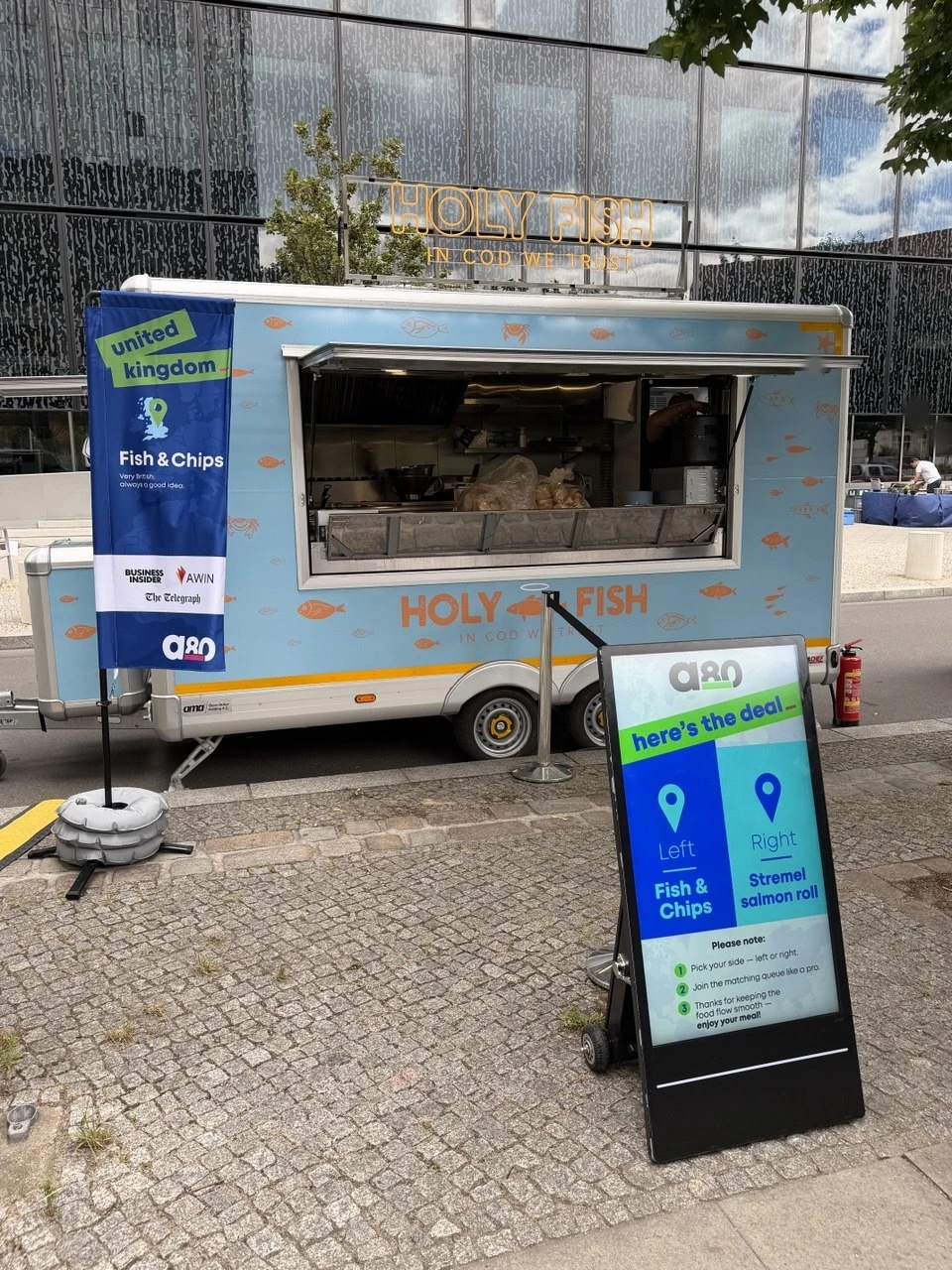 Vollständig gebrandeter Holy Fish Trailer mit Partnerfahne und digitalem Leitsystem bei der OMR; sichtbare Gesichter sind anonymisiert